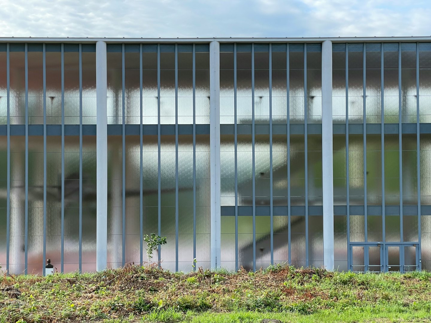 Modern industrial building with frosted glass facade and grey doors.